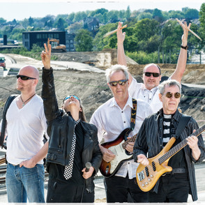 Bandfoto "Empire Rock Building" auf einer Stra&szlig;e vor einer Baustelle, mit Instrumenten
