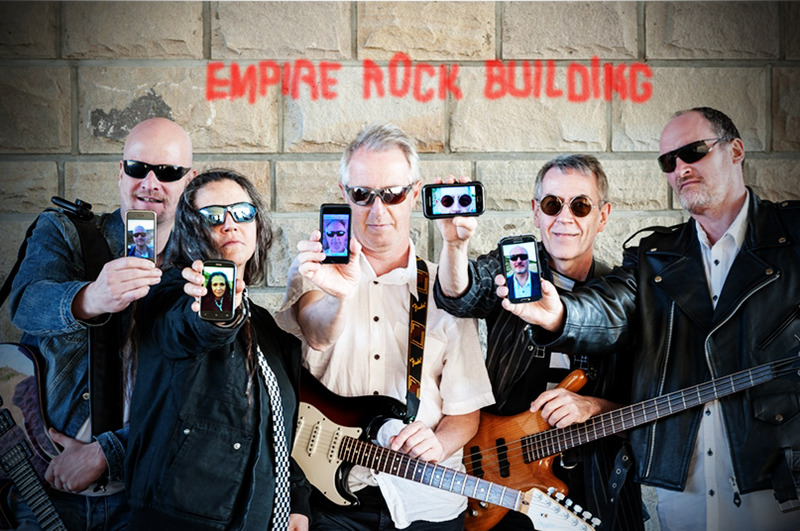 Bandfoto "Empire Rock Building" vor Sandsteinmauer, alle haben ein Handy mit Foto von sich in den Händen