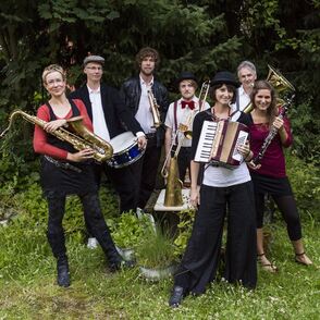 Kozma Orkesta posiert in einem Garten mit Instrumenten