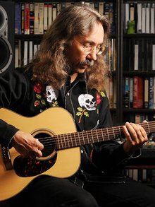 Peter Burssch mit Gitarre vor einem Bücherregal