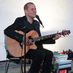 Der Künstler im Konzert auf einem Stuhl mit Gitarre